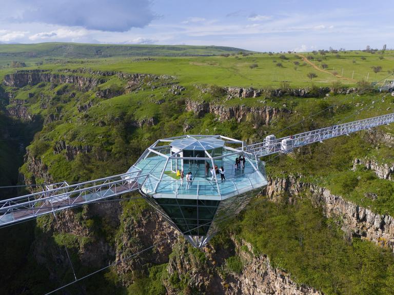 Eine Glasplattform in Diamantform mit Menschen darauf, die eine grüne Schlucht überspannt. Die Diamantenbrücke, in Georgien, die weltweit längste freihängende Konstruktion in einem Naturschutzgebiet.