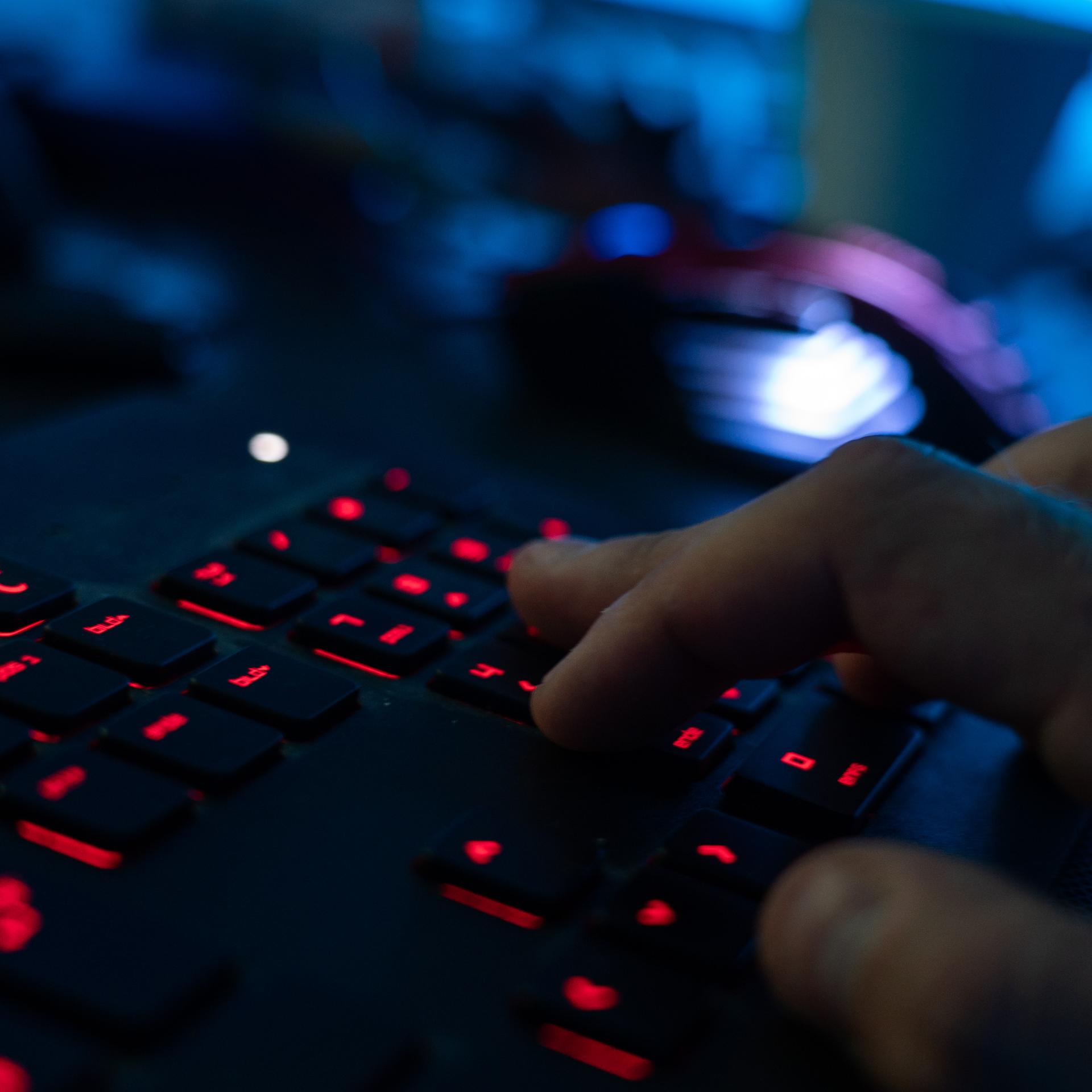 Eine Hand tippt am Rechner auf einer erleuchteten Tastatur.