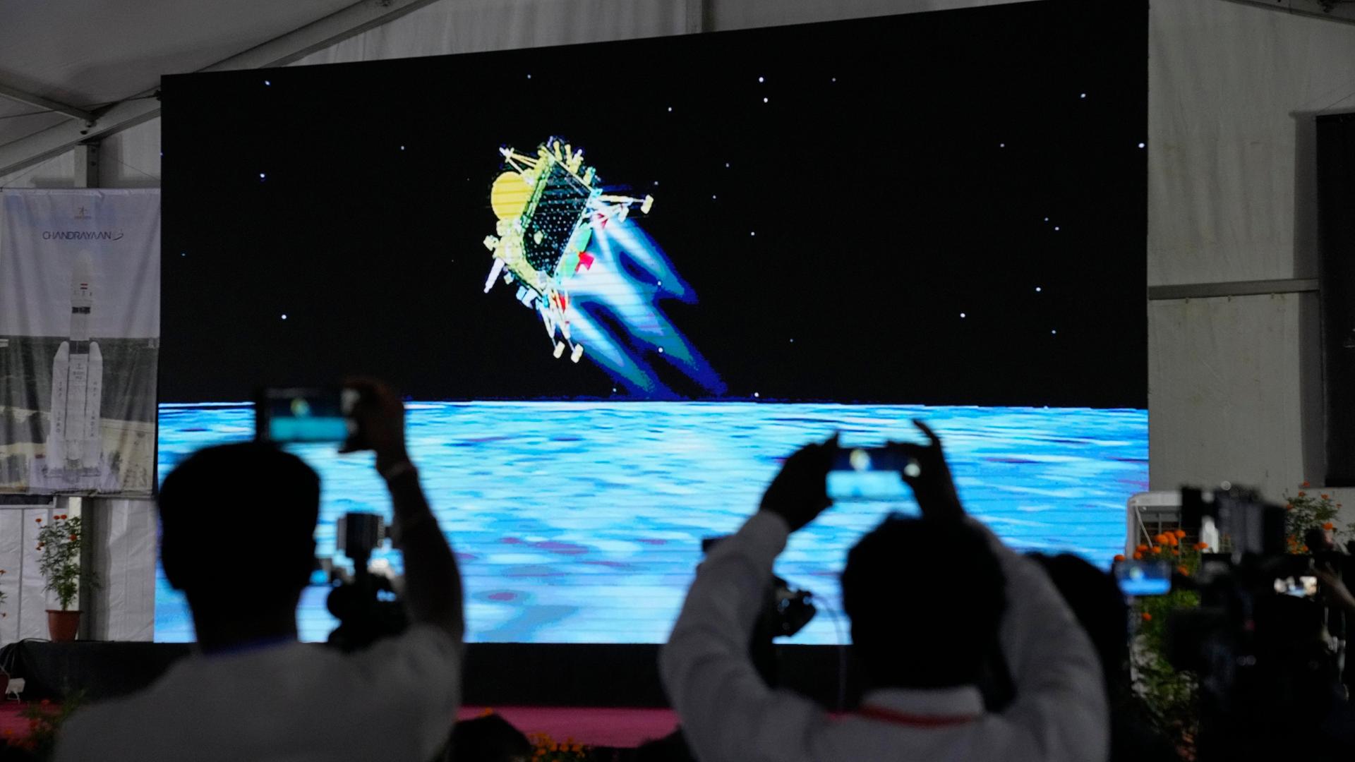 Indien, Bengaluru: Journalisten filmen die Live-Übertragung der Landung des Raumschiffs "Chandrayaan-3" auf dem Mond in der ISRO-Einrichtung für Telemetrie, Ortung und Kommandonetz.