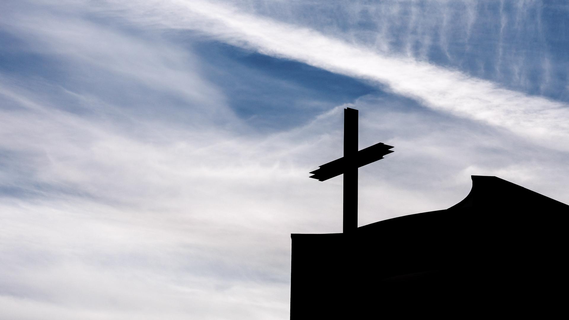 Ein Kreuz auf einer Kirche im Gegenlicht