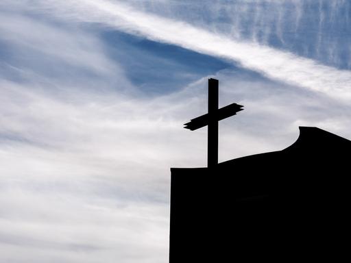 Ein Kreuz auf einer Kirche im Gegenlicht