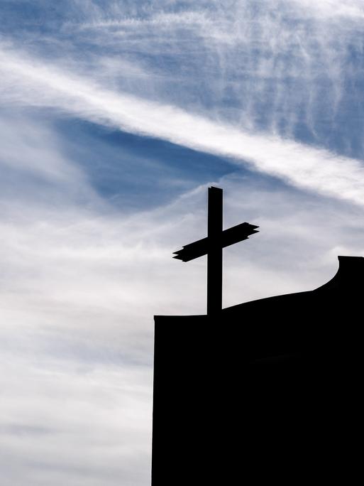 Ein Kreuz auf einer Kirche im Gegenlicht