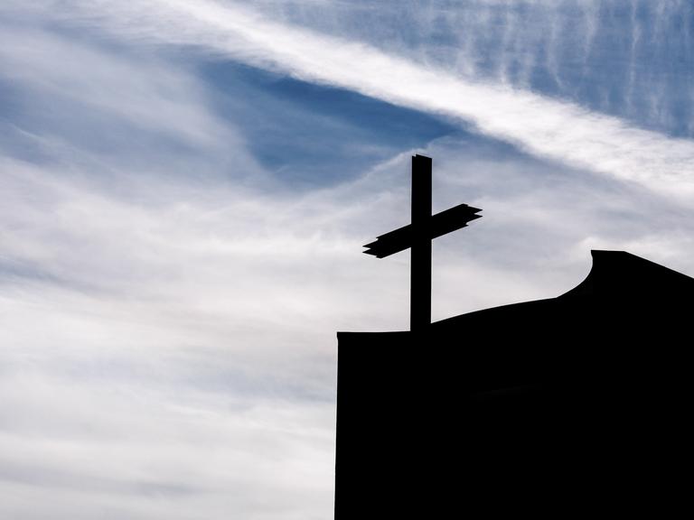 Ein Kreuz auf einer Kirche im Gegenlicht
