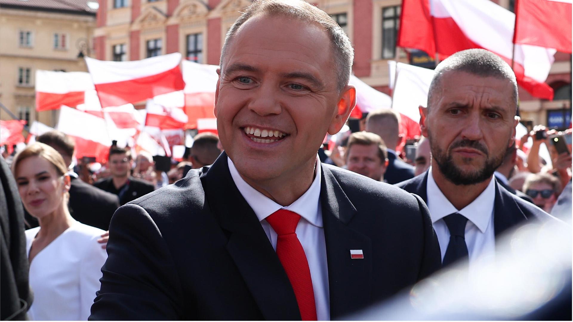 Der polnische Präsident Karol Nawrocki begrüßt Menschen mit einem Lächln. Im Hintergrund sind rot-weiße polnische Fahnen zu sehen.