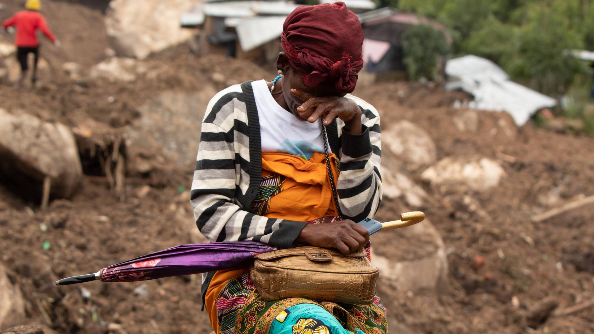 Eine Frau weint in einem vom Zyklon betroffenen Gebiet in Blantyre, Malawi im März 2023. Hinter ihr die zerstörte Stadt, Dächer und Hausteile liegen im Matsch. Eine Frau weint in einem vom Zyklon betroffenen Gebiet in Blantyre, Malawi im März 2023. Hinter ihr die zerstörte Stadt, Dächer und Hausteile liegen im Matsch.