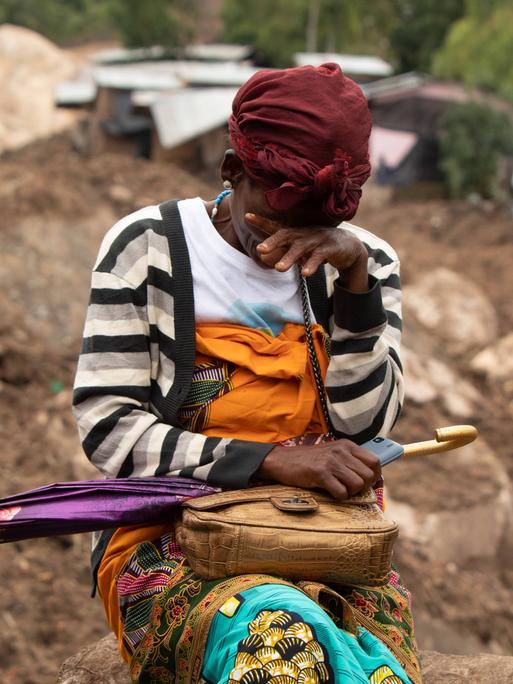 Eine Frau weint in einem vom Zyklon betroffenen Gebiet in Blantyre, Malawi im März 2023. Hinter ihr die zerstörte Stadt, Dächer und Hausteile liegen im Matsch.