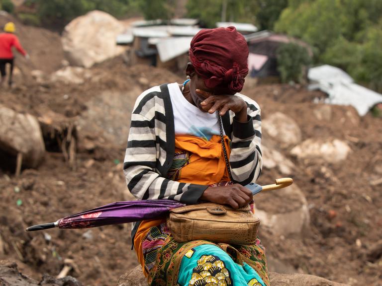 Eine Frau weint in einem vom Zyklon betroffenen Gebiet in Blantyre, Malawi im März 2023. Hinter ihr die zerstörte Stadt, Dächer und Hausteile liegen im Matsch.