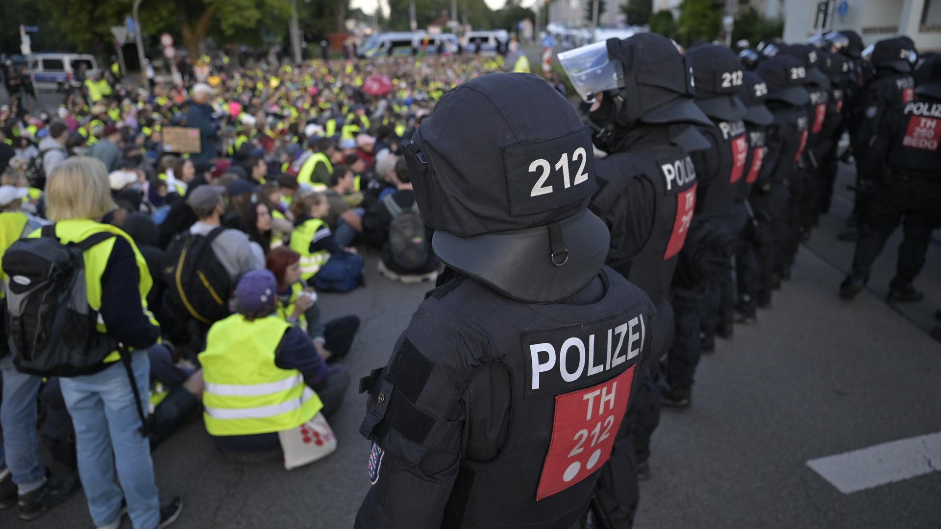 Eine Polizeikette umringt eine Menschenmenge, die auf einer Straßenkreuzung sitzt.
