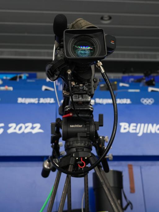 Eine Fernsehkamera steht vor den Logos der Olympischen Winterspiele von Peking 2022