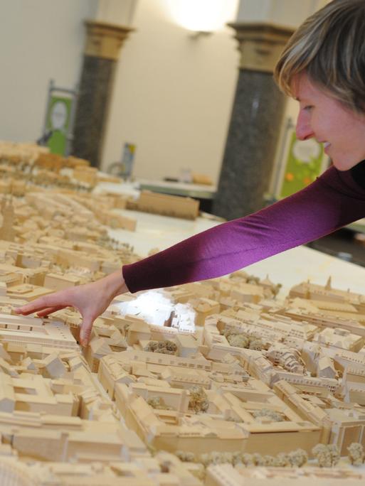 Eine Modellbauerin setzt ein Gebäude in ein hölzernes Modell der Münchener Altstadt ein.