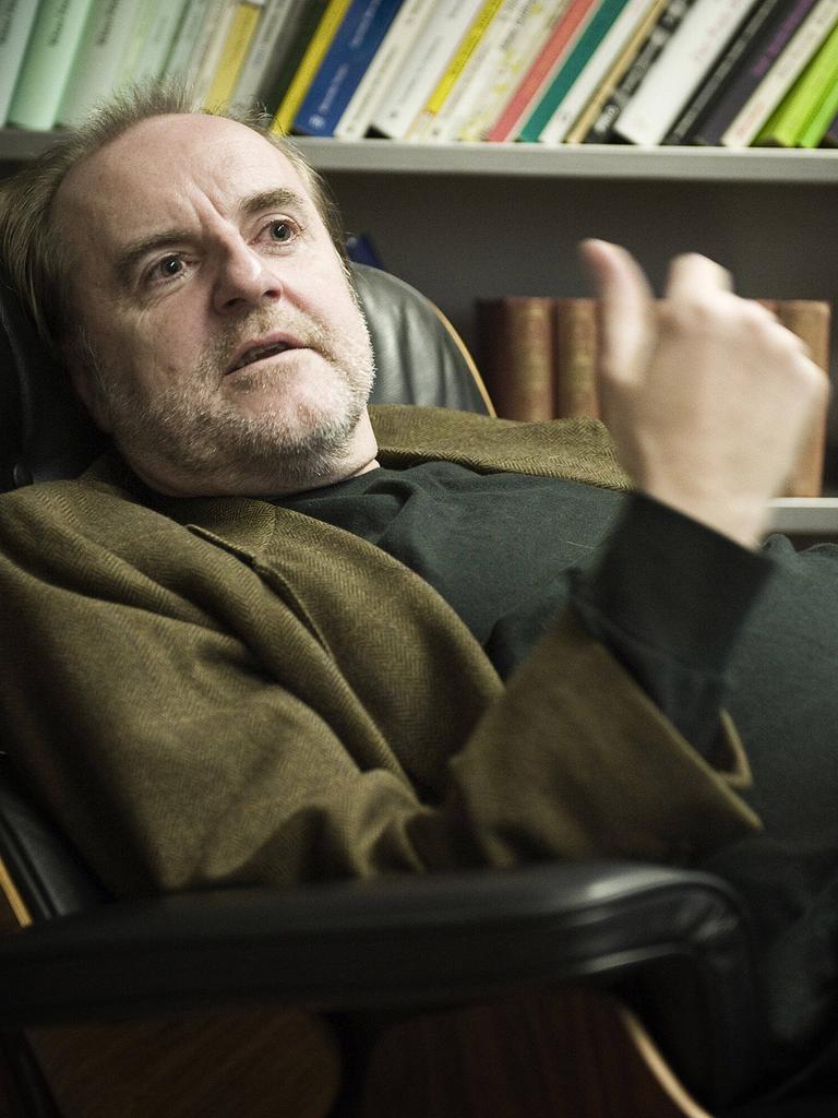 Peter Schneider sitzt in seiner Praxis bequem in einem Lehnsessel, hinter sich ein gut gefülltes Bücherregal.