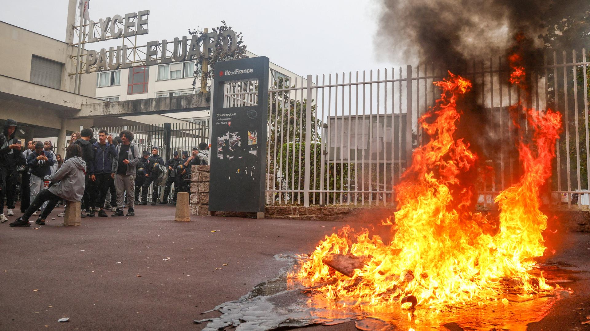 Das Bild zeigt ein Feuer. Im Hintergrund steht ein Schul-Gebäude.