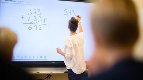 Lehrerin schreibt vor vierter Klasse eine Mathematikaufgabe an die Tafel