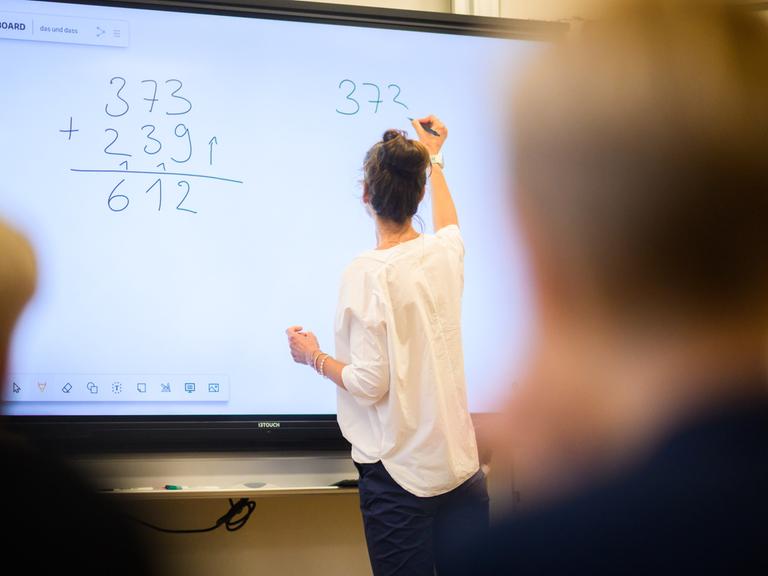 Lehrerin schreibt vor vierter Klasse eine Mathematikaufgabe an die Tafel