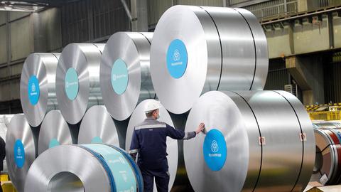 In einem Stahlwerk schaut sich ein Mitarbeiter große Spulen aus Stahl an. 
