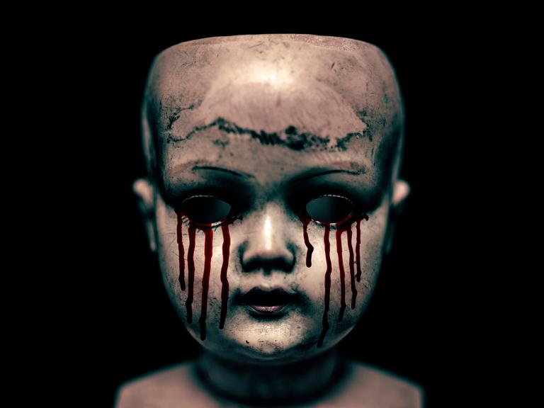 Ein gruseliger Puppenkopf mit blutenden Augen vor schwarzem Hintergrund