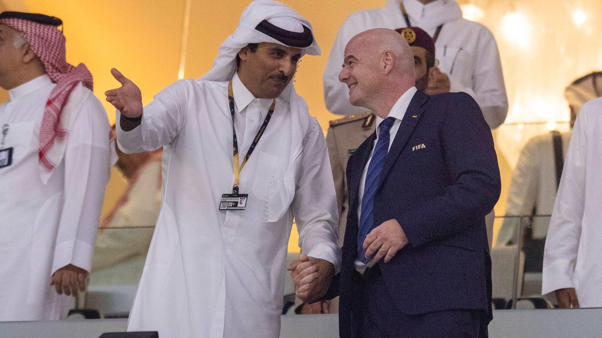 Der FIFA-Präsident Gianni Infantino steht Hand in Hand mit dem Emir von Katar in einem Fußball-Stadion.