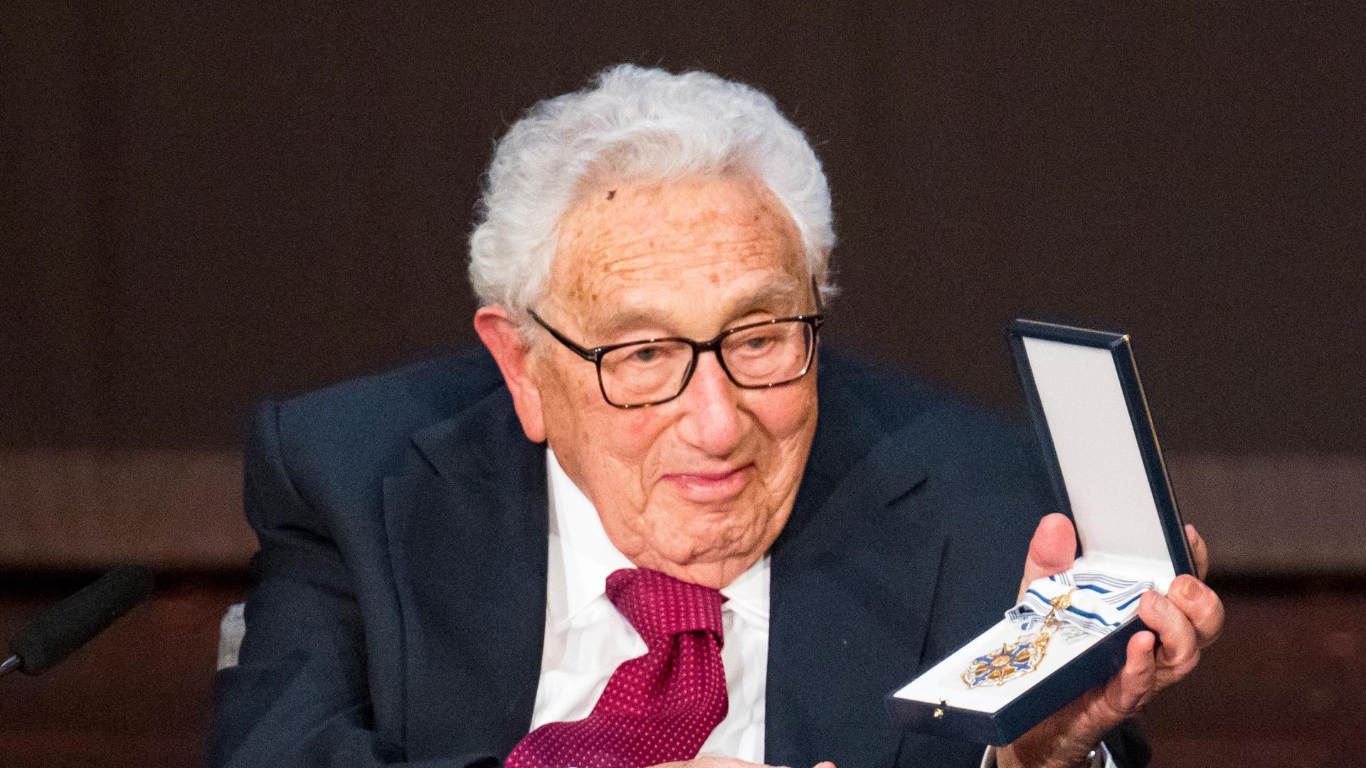 Henry Kissinger bei der Feier zu seinem 100. Geburtstag. In seiner linken Hand hält er einen Orden in einer Schachtel.
