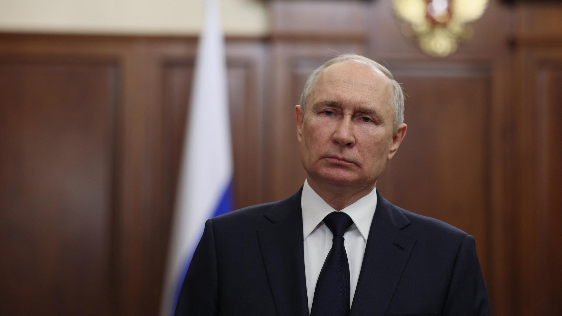 Russlands Präsident Putin steht vor einer holzvertäfelten Wand im Kreml. Er trägt einen dunklen Anzug, eine Krawatte und ein weißes Hemd und schaut ernst.