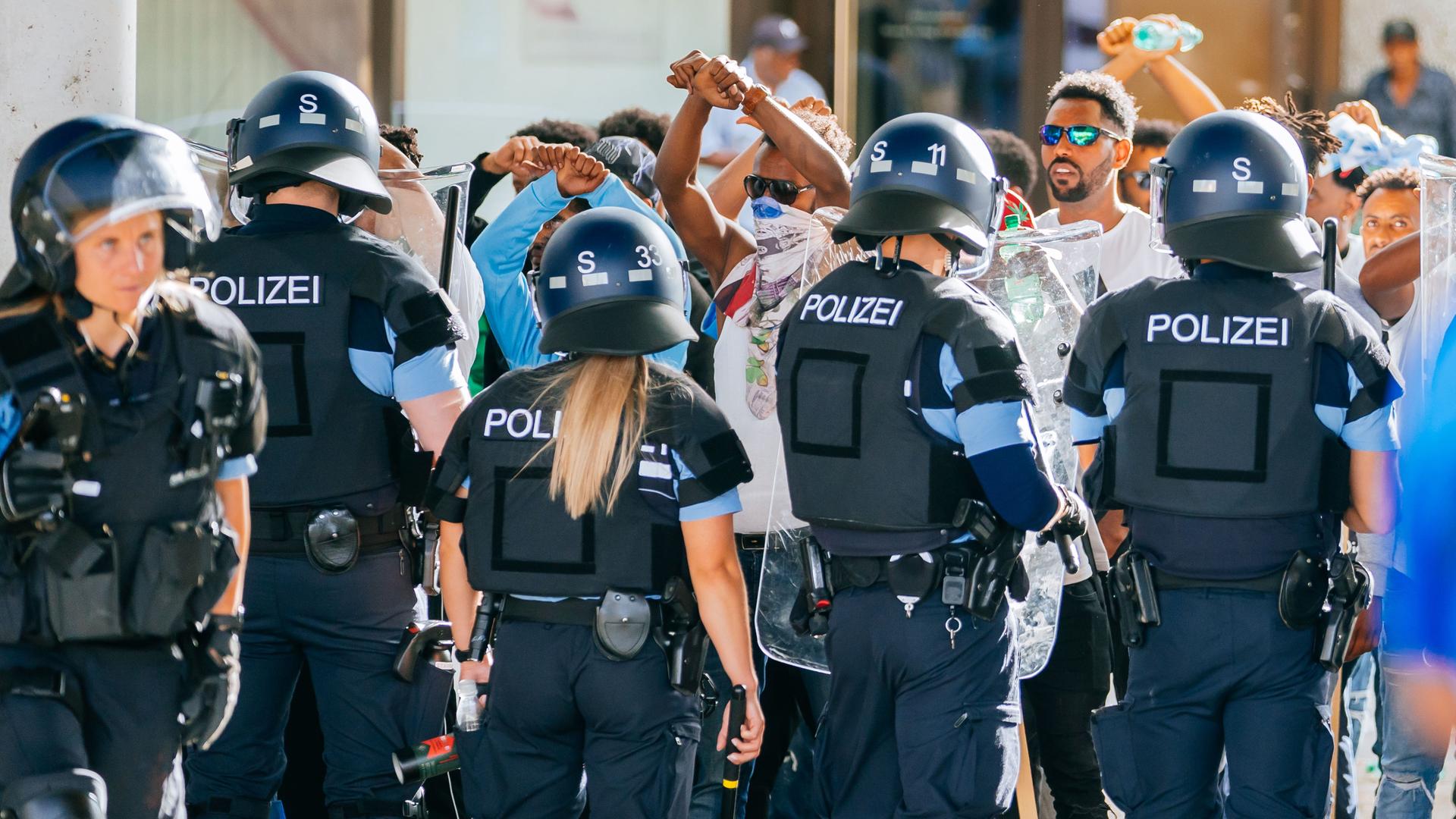 Eine Gruppe von Menschen wird nach Ausschreitungen bei einer Eritrea-Veranstaltung von Polizeikräften in Schutzkleidung in Schach gehalten