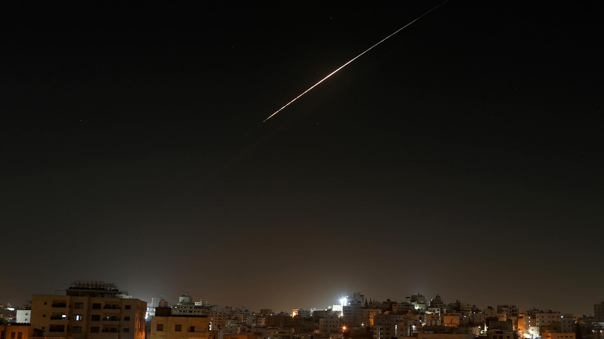 Eine Stadt bei Nacht, am Himmel ist der helle Schweif einer Rakete zu sehen. Eine Stadt bei Nacht, am Himmel ist der helle Schweif einer Rakete zu sehen.