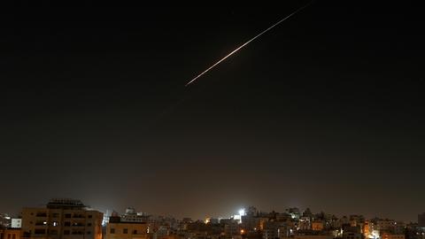 Eine Stadt bei Nacht, am Himmel ist der helle Schweif einer Rakete zu sehen.