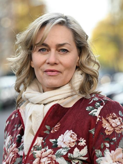 Die Schauspielerin Gesine Cukrowski steht bei einem Fototermin in ihrem Kiez. Sie trägt eine geblümte Jacke und einen beigen Schal. Der Hintergrund ist verschwommen.