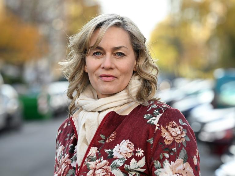 Die Schauspielerin Gesine Cukrowski steht bei einem Fototermin in ihrem Kiez. Sie trägt eine geblümte Jacke und einen beigen Schal. Der Hintergrund ist verschwommen.