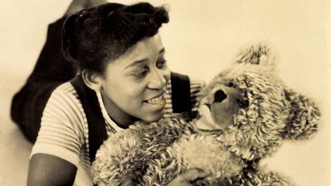 Historisches Sepiafoto von Leila Negra, die mit einem Teddybären auf dem Boden liegt.