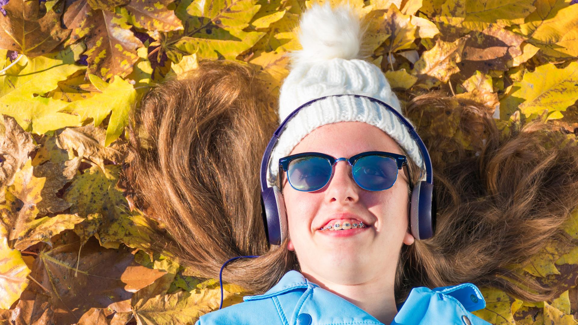 Mädchen liegt im Herbstlaub und hört mit Kopfhörern