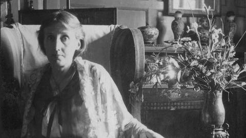 Virginia Woolf sitzt in einem Sessel neben einem Blumenstrauß.