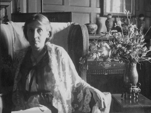 Virginia Woolf sitzt in einem Sessel neben einem Blumenstrauß.