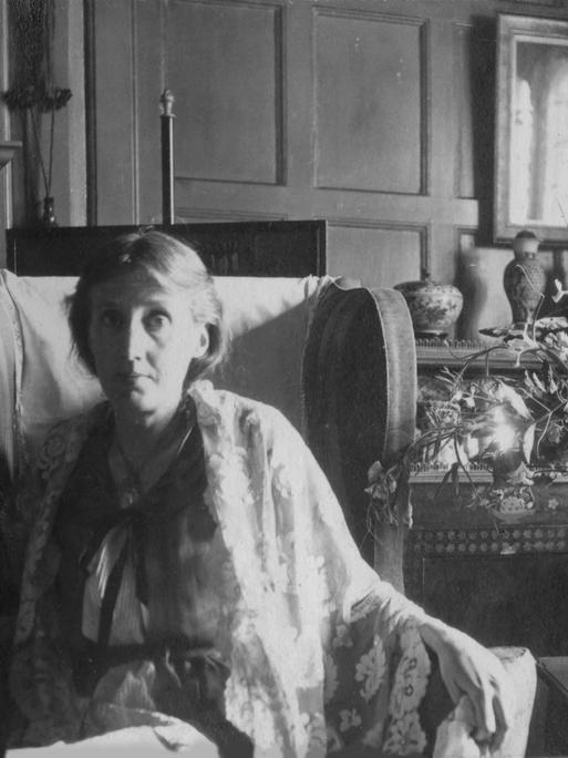 Virginia Woolf sitzt in einem Sessel neben einem Blumenstrauß.