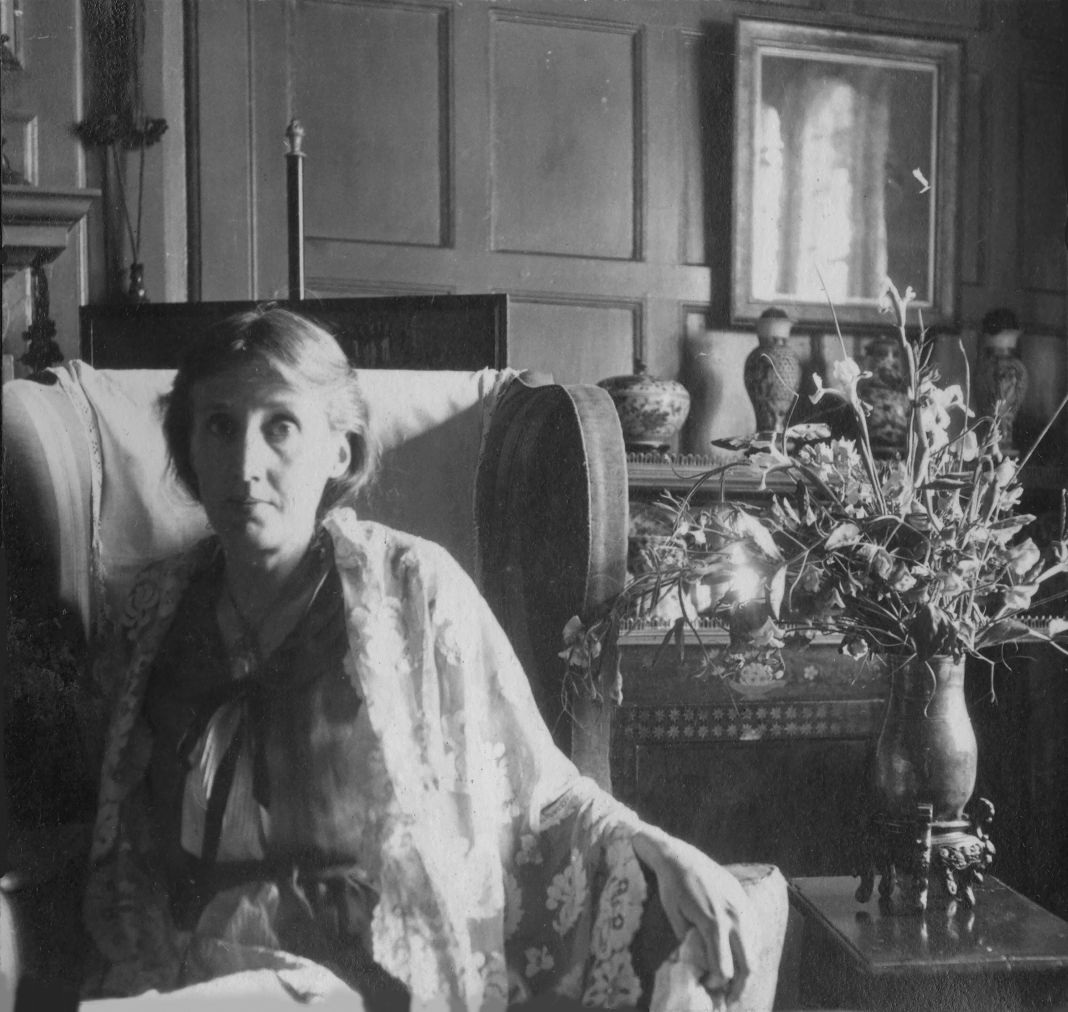 Virginia Woolf sitzt in einem Sessel neben einem Blumenstrauß.