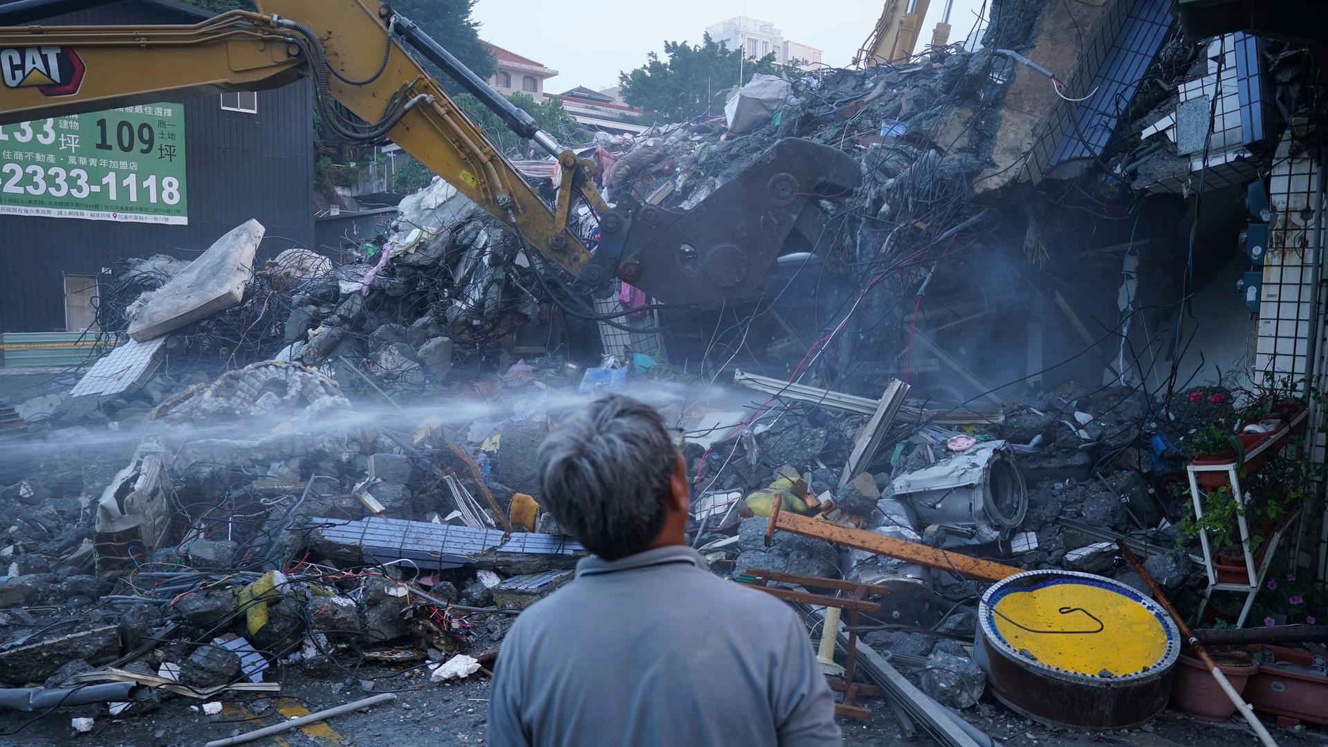 Ein Mann steht vor einem Schutthaufen zerstörter GEbäudeteile nach dem schweren Erdbeben in Taiwan. Ein Kran ist im Einsatz. 