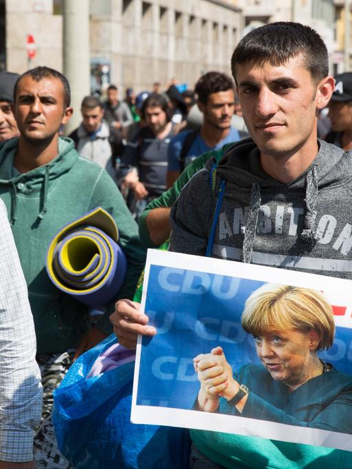 Einige Flüchtlinge tragen Fotos der deutschen Bundeskanzlerin Angela Merkel als sie vom Bahnhof Keleti losmarschieren. Budapest, Ungarn - 04.09.2015 