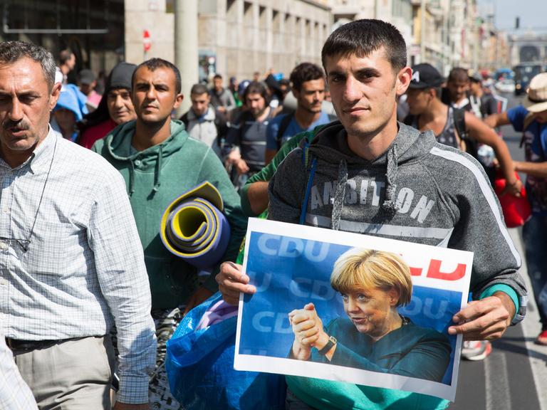 Einige Flüchtlinge tragen Fotos der deutschen Bundeskanzlerin Angela Merkel als sie vom Bahnhof Keleti losmarschieren. Budapest, Ungarn - 04.09.2015 
