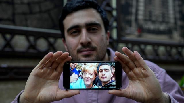 Anas Modamani hält ein Handy mit seinem Selfie mit Angela Merkel mit zwei Händen vor seinem Körper.