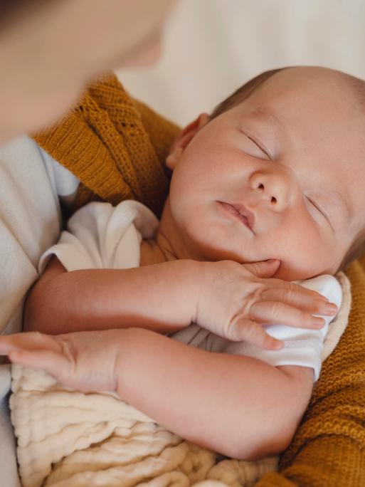 Das Foto zeigt ein schlafendes Baby im Arm seiner Mutter.