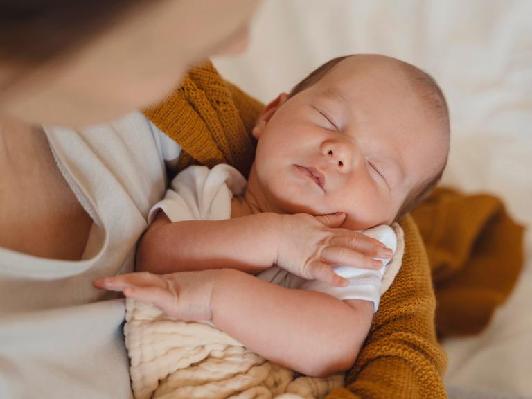 Das Foto zeigt ein schlafendes Baby im Arm seiner Mutter.