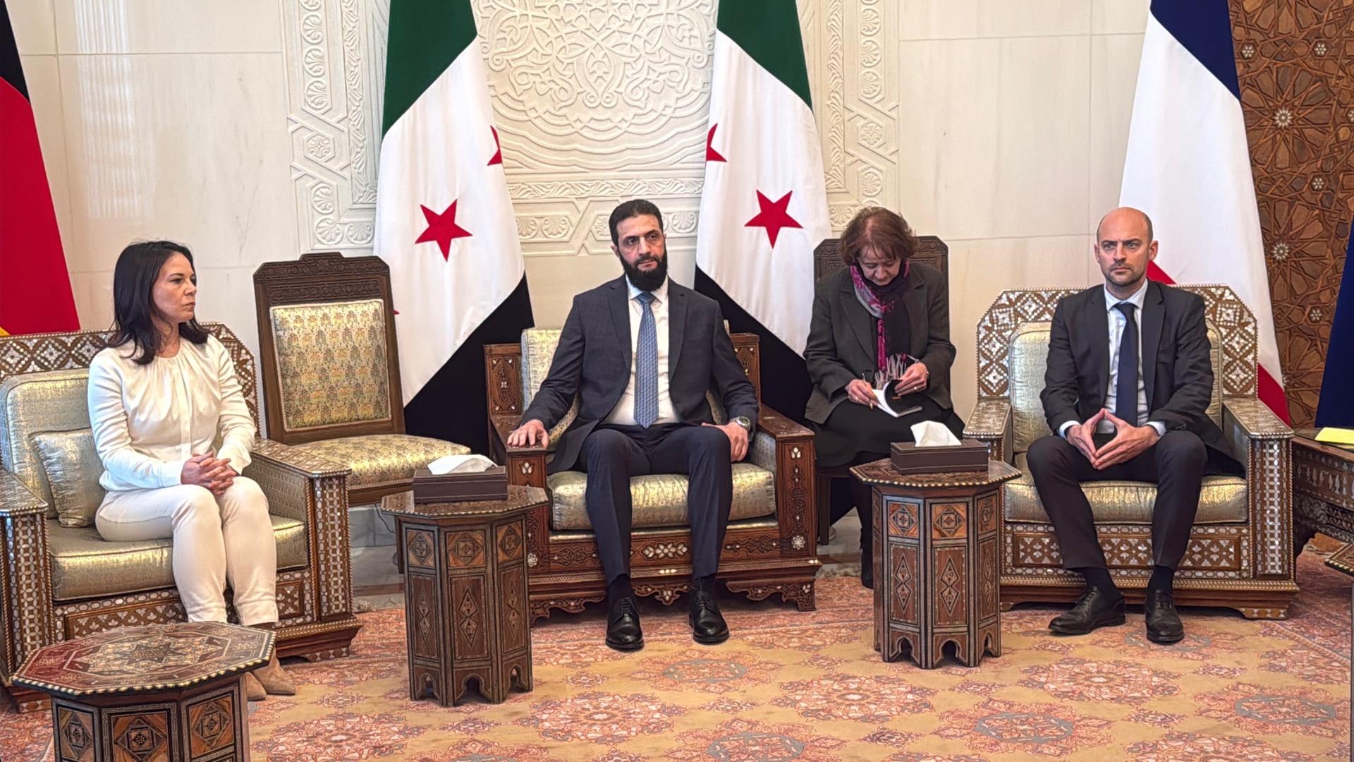 Bundesaußenministerin Baerbock (links), ihr französischer Amtskollege Barrot (rechts) und der neue syrische Machthaber al-Scharaa (Mitte) sitzen nebeneinander auf Sesseln.