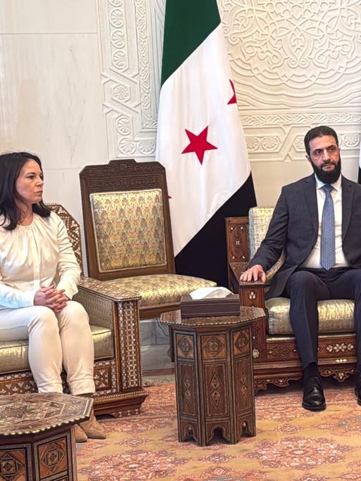 Bundesaußenministerin Baerbock (links), ihr französischer Amtskollege Barrot (rechts) und der neue syrische Machthaber al-Scharaa (Mitte) sitzen nebeneinander auf Sesseln.