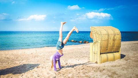 Ein Kind macht am Strand neben einem Strandkorb einen Handstand. Ein Kind macht am Strand neben einem Strandkorb einen Handstand.