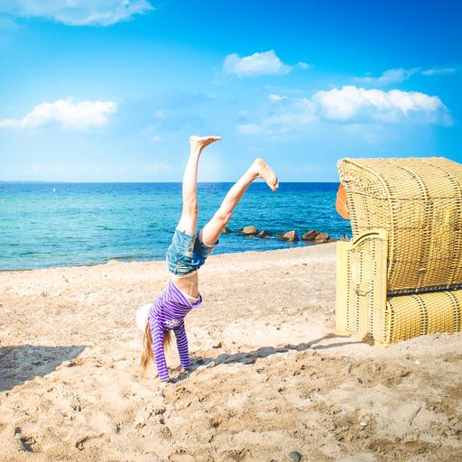 Ein Kind macht am Strand neben einem Strandkorb einen Handstand.