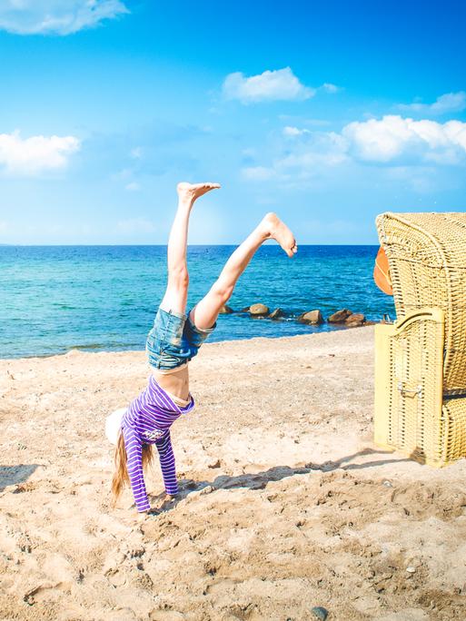 Ein Kind macht am Strand neben einem Strandkorb einen Handstand.