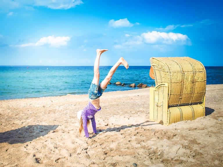 Ein Kind macht am Strand neben einem Strandkorb einen Handstand.