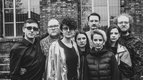 Die acht Mitglieder des Ensembles stehen auf einem schwarz-weiß-Foto eng beieinander.