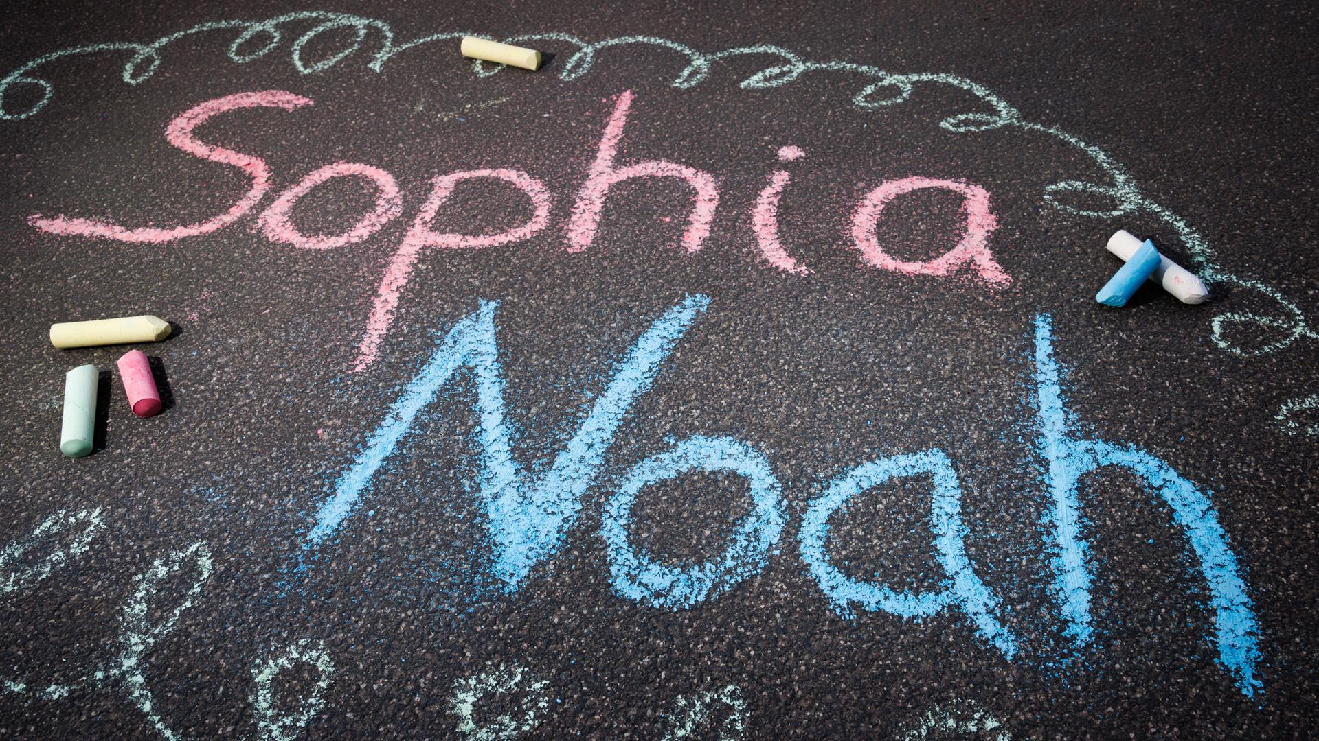 Mit Straßenkreide sind die Namen Sophia und Noah auf den Boden geschrieben. Mit Straßenkreide sind die Namen Sophia und Noah auf den Boden geschrieben.