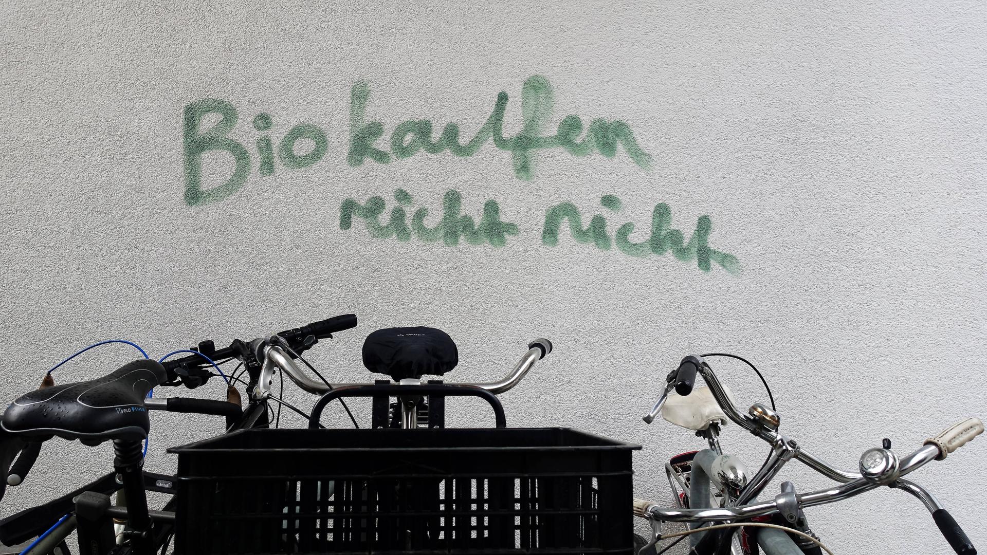 Auf einer Hauswand steht ein Graffito: "Bio kaufen reicht nicht", im Vordergrund sind Fahrräder zu sehen.