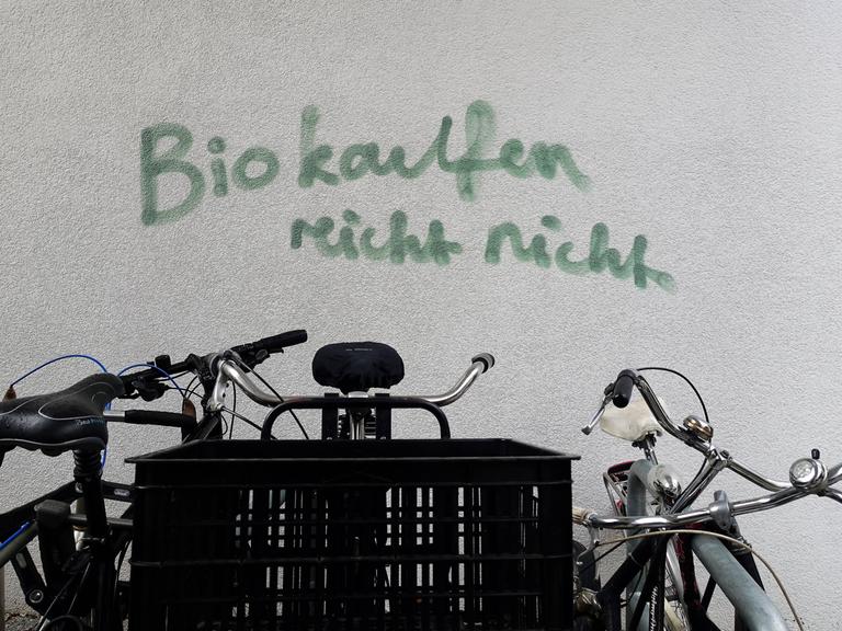 Auf einer Hauswand steht ein Graffito: "Bio kaufen reicht nicht", im Vordergrund sind Fahrräder zu sehen.